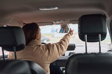 Woman adjusting her rearview mirror inside a car, ensuring clear visibility for safe and focused...