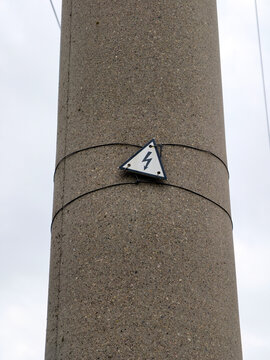 Warning lightning sign attached to industrial concrete pole marking dangerous electrical power line