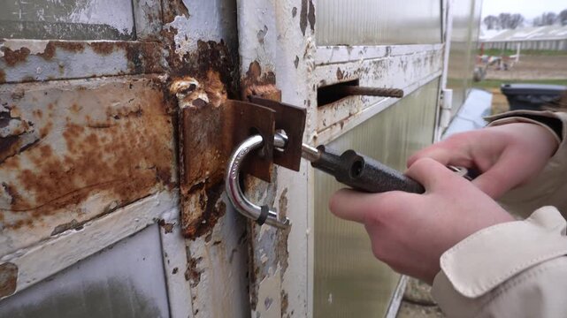 The girl closes the lock with a key. Hands in close-up. The rusty gate is locked with a padlock. The concept of security and access.