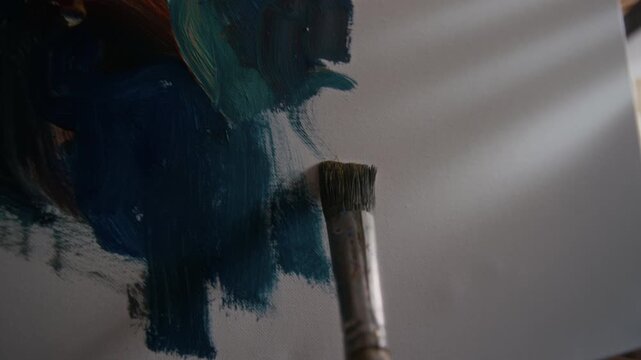 POV close up shot of brush applying oil paint strokes to canvas, creating abstract painting during artistic process