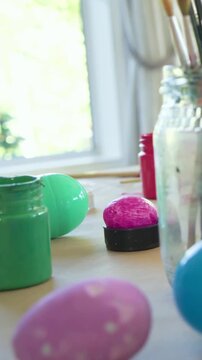 Vertical video: Panning camera revealing craft table near window, showing painted eggs and brushes