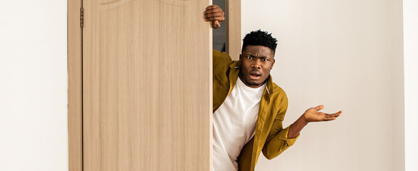 A person stands next to an open door with a surprised expression. They are wearing a casual outfit. The room has plain walls and minimal furniture, focusing on the person's reaction. © Prostock-studio