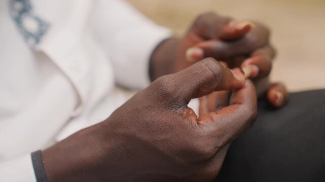 Black man hands fidgeting romantic date. Closeup of dark skin fingers and embroidered cuff, subtle clasping and nervous motion. Warm shallow focus creates intimate candid mood, hint of anticipation