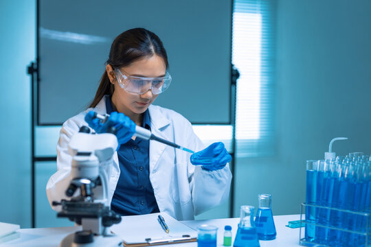 Young Asian scientist conducting research, dropping liquid into a petri dish, surrounded by lab equipment and blue solutions