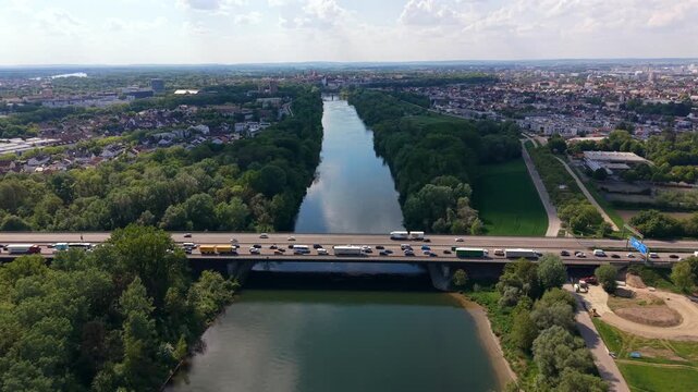 Aerial scene of Autobahn 9 bridge crossing the Danube shows long vehicle queues caused by construction. Cars and trucks move slowly through the Ingolstadt area surrounded by forests and riverbanks.