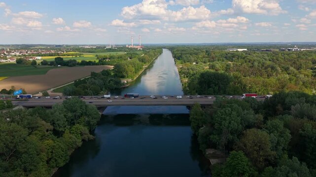 Aerial view of Autobahn 9 near Ingolstadt shows heavy slow moving traffic on Danube bridge. Cars and trucks form long queue caused by road reconstruction, surrounded by Bavarian forests and river