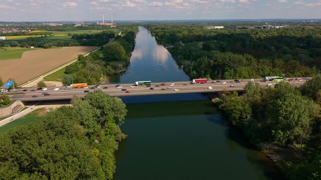 Drone footage captures heavy congestion on Autobahn 9 Danube crossing. Cars and trucks queue for kilometers due to lane closures, set against the natural landscape of Upper Bavaria near Ingolstadt.