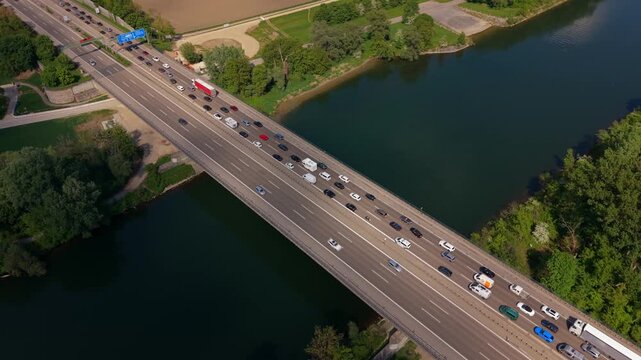 Aerial panorama of A9 highway bridge over Danube reveals long queues of cars and trucks. Roadworks create bottleneck as traffic moves slowly through the Ingolstadt region in sunny Bavarian scenery.