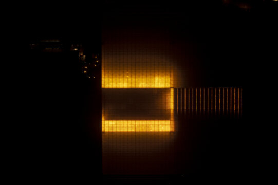 Aerial view of a large glowing greenhouse complex at night with bright orange lights illuminating the rectangular structure.