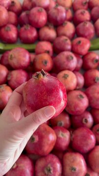 Hand picks ripe red pomegranate from abundant market display of fresh organic fruit in natural selection gesture. Antioxidant fruit footage suits grocery retail promotion, juice brand content