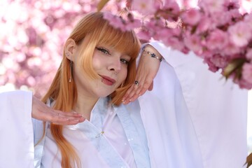 Naklejka premium Beautiful young girl in kimono posing near blossoming sakura tree outdoors