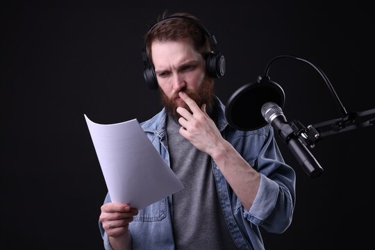 Voice actor with headphones and script performing on black background