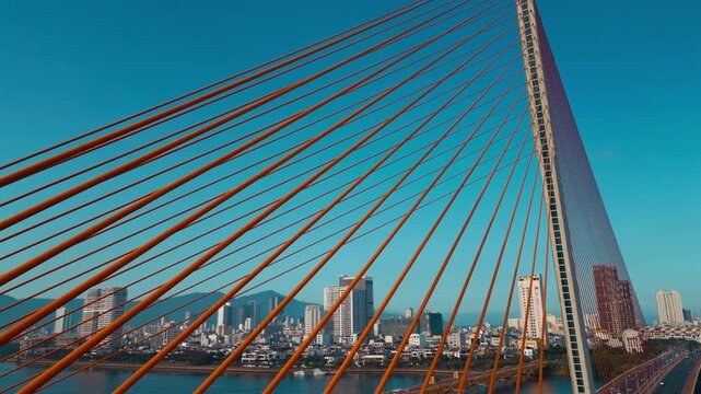 aerial drone view of suspension cable bridge over Han river in Danang, geometric cable-stayed bridge architecture with modern city skyline and roadway, Da Nang Vietnam 4k