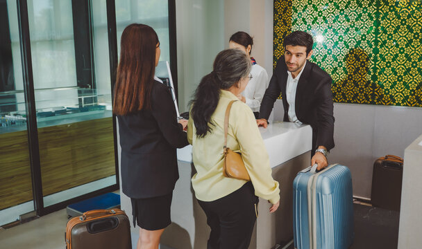 Business travelers and senior woman standing at airport check in counter with airline staff and luggage