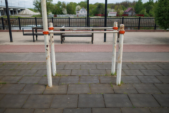 Front view of old metal parallel bars in a city park with a river and houses in the distance