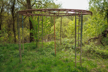 Fototapeta premium Large circular metal jungle gym in a wooded area with rusty ladders and hanging rings