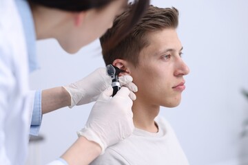 Fototapeta premium Hearing test. Doctor examining man's ear with otoscope in clinic, closeup