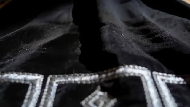 Camera pulling back after nudge, revealing black velvet silver motif on wood table showing detail