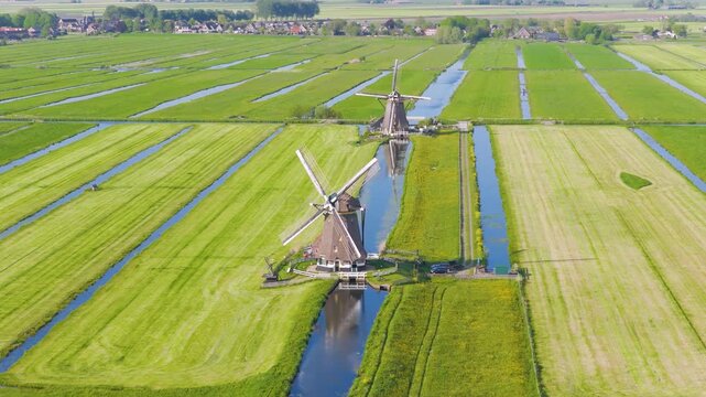 Aerial view of traditional Dutch windmills near water canals in a green field. Clear sunny day with reflections on the water surface and a wide video landscape captured by drone.