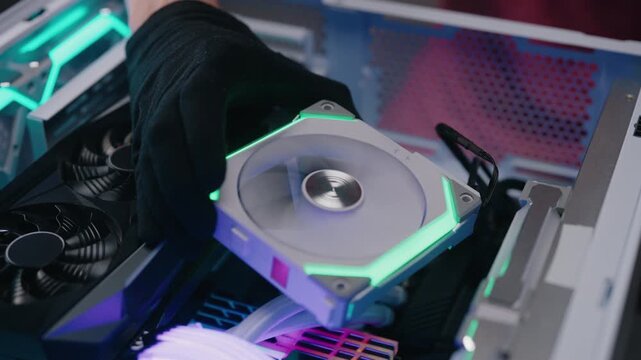 Gloved hand of technician installing high performance rgb cooling fan into custom gaming computer case, ensuring proper airflow and thermal regulation for peak system efficiency, closeup, slow motion.