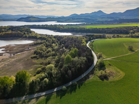 Aerial view of a winding road through green fields and forest near the Liptovska Mara reservoir with mountains in the distance Liptovsky Trnovec, Zilina Region, Slovakia.