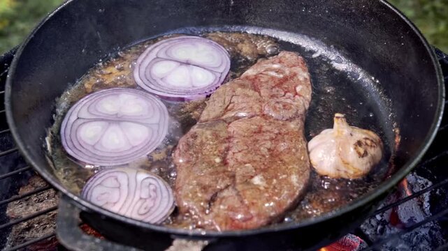 Brown Steak Sizzling With Purple Onion, Garlic Bulb And Butter Baste, Juicy Beef Fibers, Smoky Pan, Campfire Ember Backdrop, Rustic Plating Ready