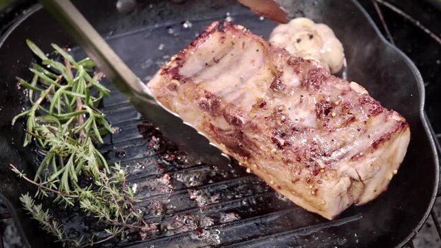 Seared Steak On Skillet With Rosemary, Tongs Press Fat Cap, Roasted Garlic Head Beside, Smoky Sizzle, Outdoor Grill Closeup, Golden Crust And Juicy Interior