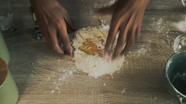 Experienced male baker kneading homemade bread dough with flour on a dark rustic wooden table.