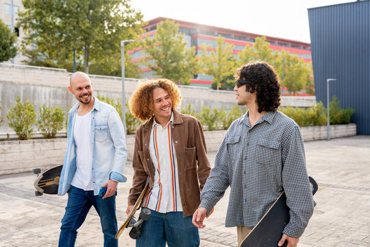 Friends with skateboards walking and talking in urban plaza