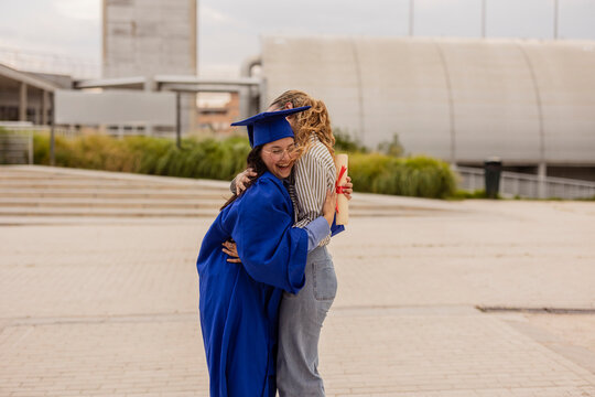 Two women hugging after graduation with diploma outdoors