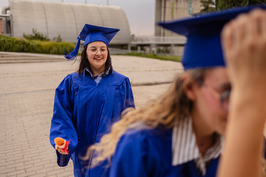 Women students in graduation gowns outdoors on campus walkway