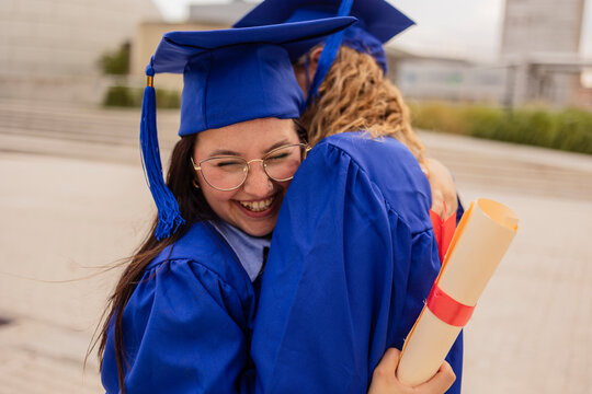 Female graduates hugging and celebrating with diploma