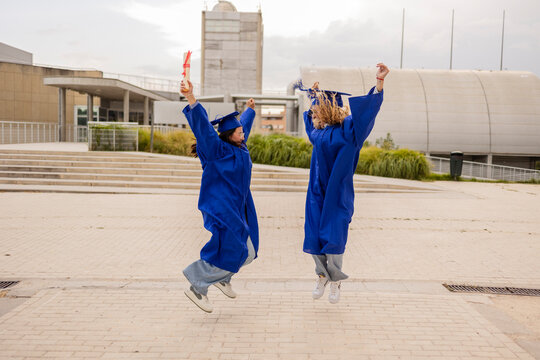 Two women students jumping in blue caps and gowns outdoors