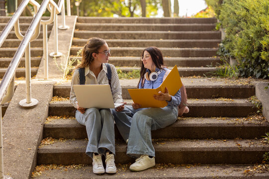 Two women students study together outdoors on campus steps