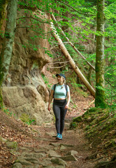 Obraz premium Woman with backpack hiking through rocky forest path surrounded by green woodland and sandstone cliffs during outdoor adventure trip