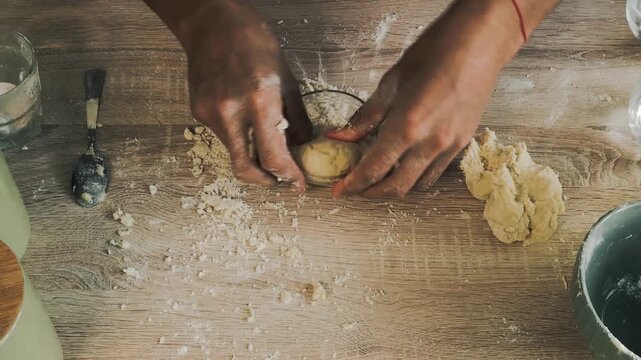 Experienced male baker kneading homemade bread dough with flour on a dark rustic wooden table.