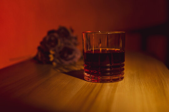 glass of whiskey by candlelight with flowers in the background, dim light