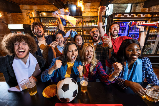 Energetic group of friends cheering during live soccer match in pub