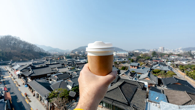 Takeaway coffee held above a traditional Korean village view