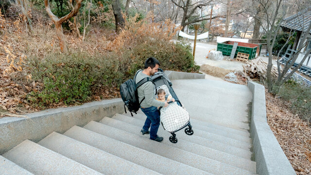Father with backpack pushing stroller down park stairs