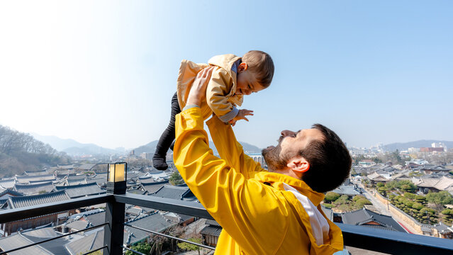 Father lifting baby on balcony with city and mountain view