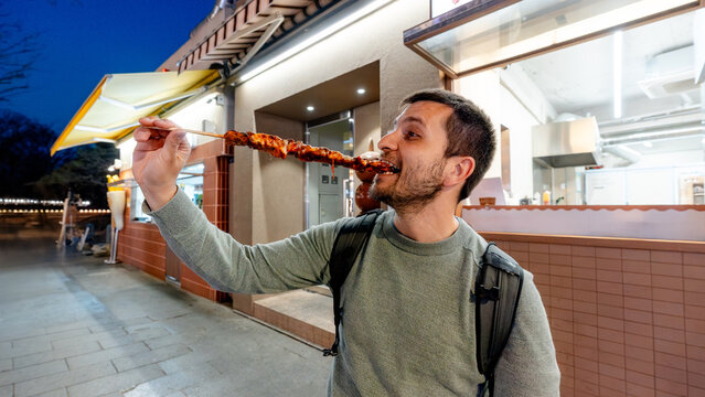 Man eating grilled skewer outside street food restaurant