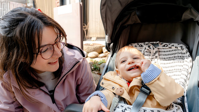 Mother with glasses smiling at baby in stroller outdoors