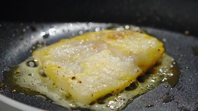 Frying white fish fillets. Frying hake fillets in a hot pan Bubbling oil melting around fillet edge, closeup of foam and gloss as fish releases juices, high heat simmering