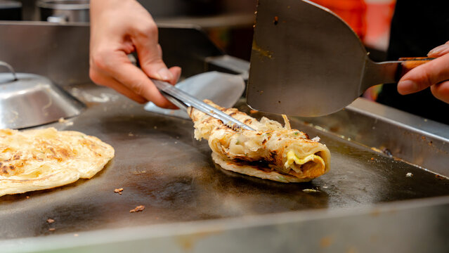 Hand of Taiwanese street food vendor cooking scallion pancake