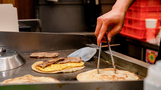 Hand of Taiwanese night market vendor cooking scallion pancake