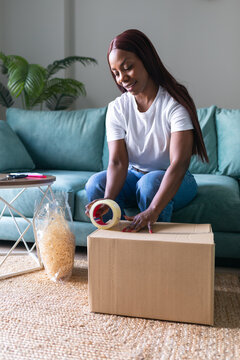 Black woman packing a box for secondhand selling app at home