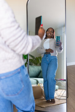 Black woman listing secondhand clothes with smartphone mirror photo