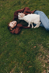 Obraz premium Cheerful woman outdoors, lying on grass, goat kid nuzzles her hand, relaxed pose, sunlit scene, natural colors, gentle breeze, countryside mood, authentic lifestyle moment, joyful connection