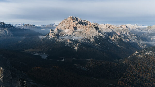 Aerial view of Monte Cristallo mountain range overlooking forested valleys and a small alpine lake under a soft sky in the Dolomites, Auronzo di Cadore, Veneto, Italy.